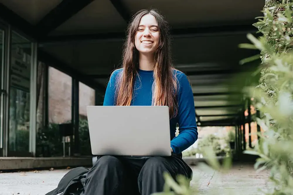 College student sitting on outdoor steps with a laptop