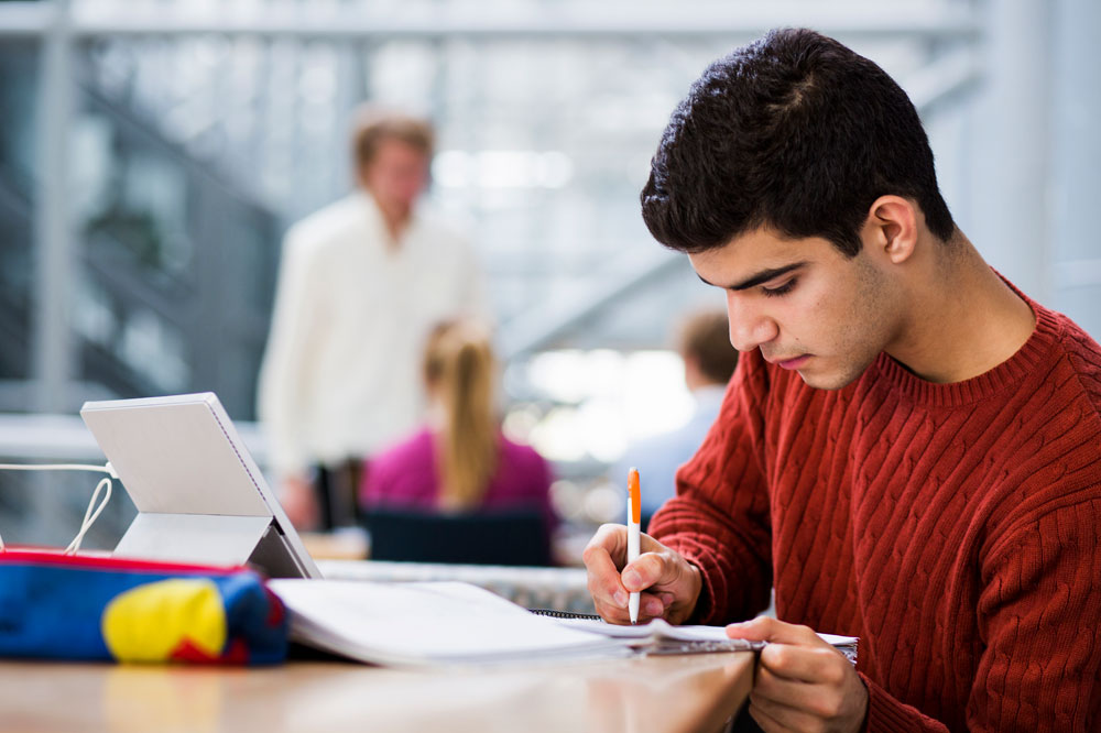 Student writing at a desk while working on a letter of intent