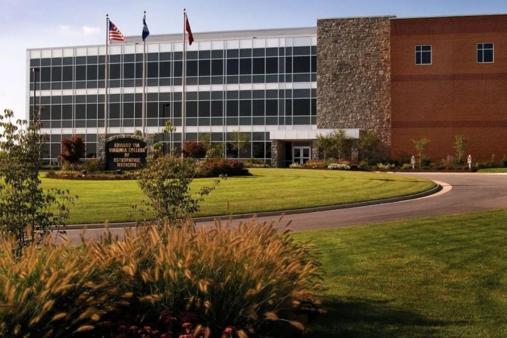 Front view of the Edward Via College of Osteopathic Medicine with 3 flags in the font of the building leading up the the door.